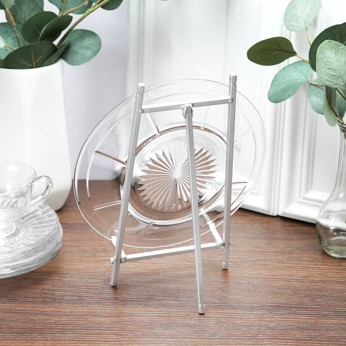 Satin silver metal easel displaying a clear glass plate on wooden surface