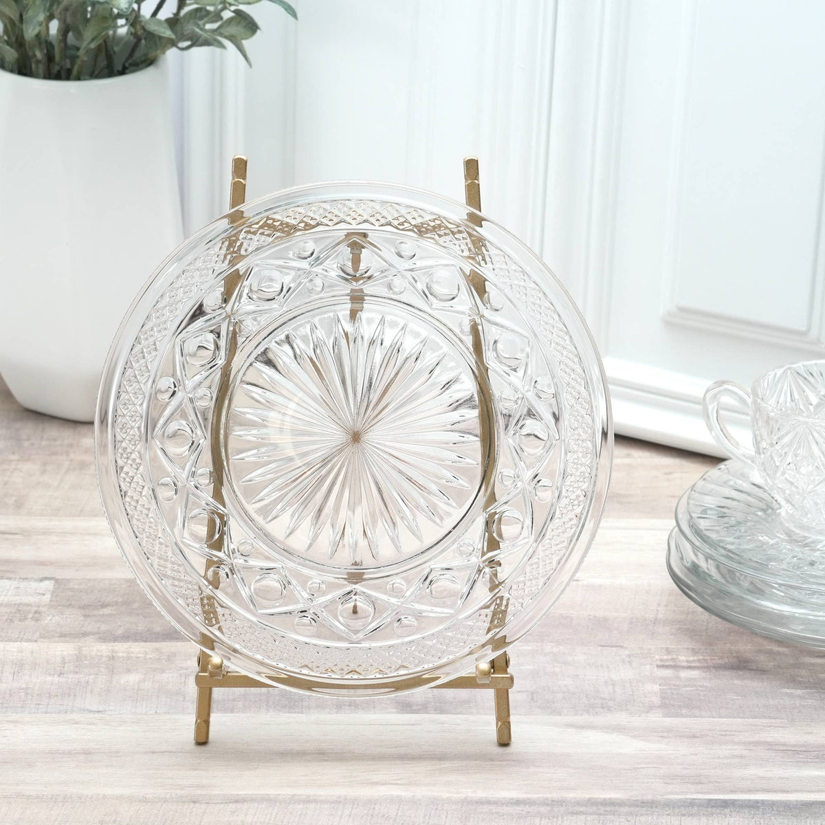 Satin gold metal plate easel displaying ornate clear crystal glass plate on wood surface