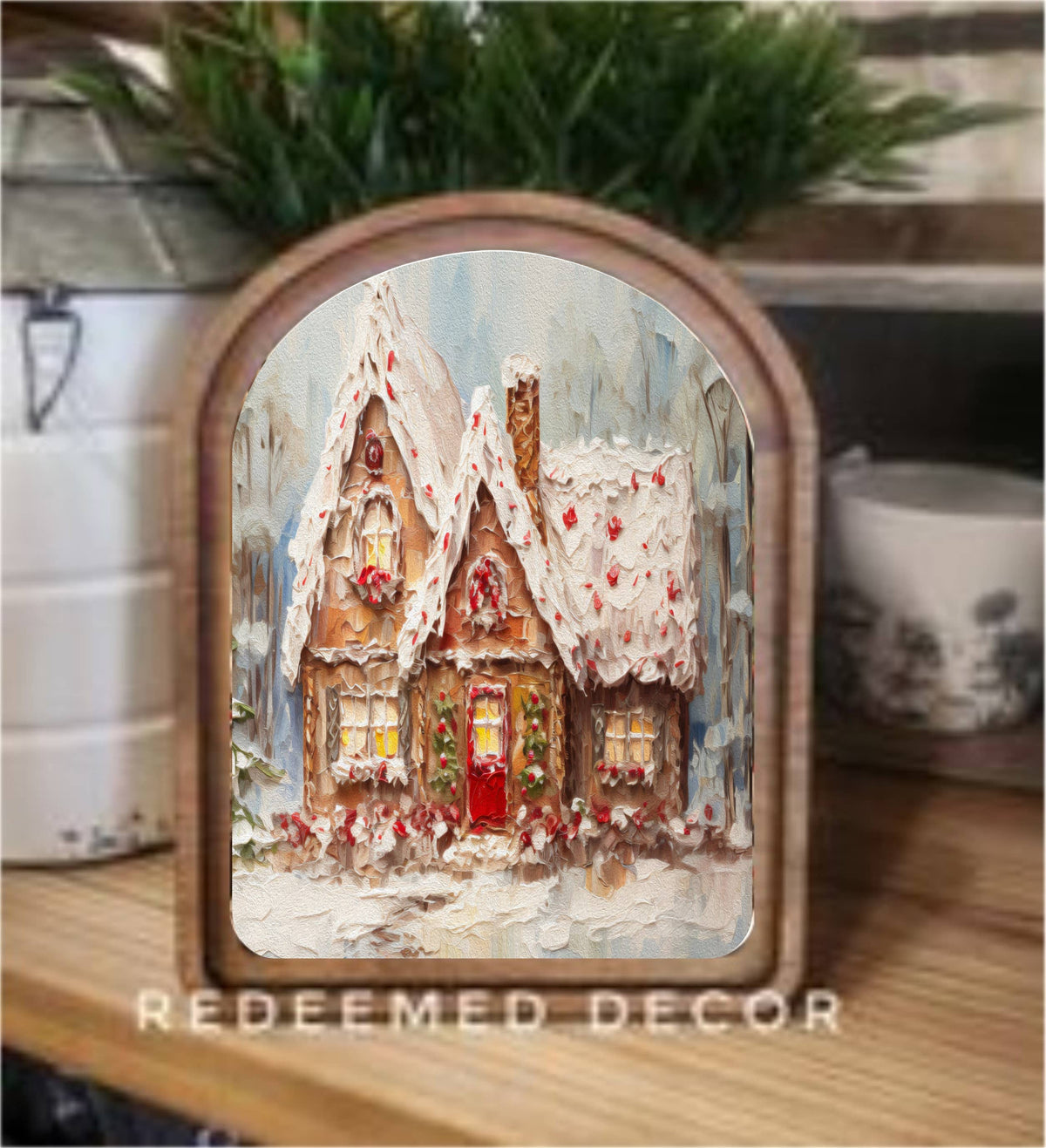 Arched wood-framed canvas print of a snowy gingerbread cottage with red door on shelf
