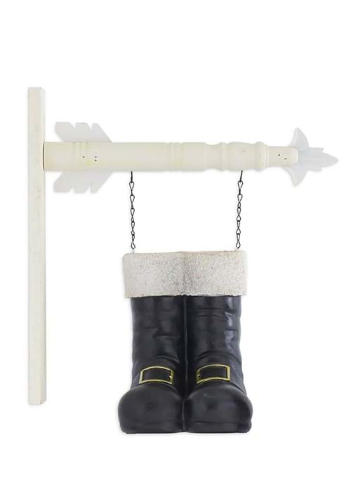 Pair of black Santa boots with white fur trim hanging from a white arrow sign via chains