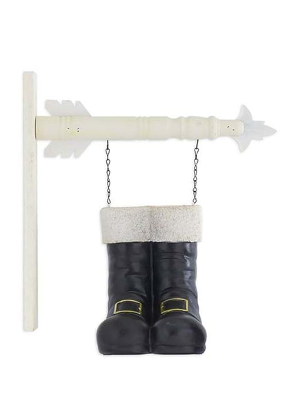 Pair of black Santa boots with white fur trim hanging from a white arrow sign via chains