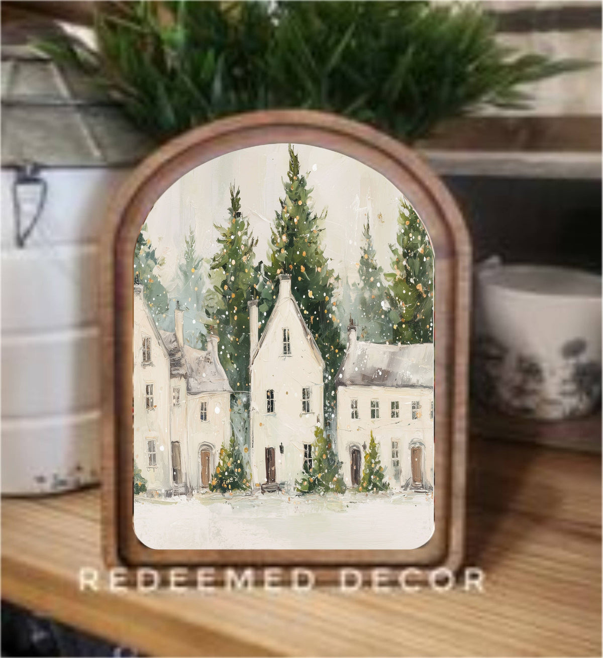 Arched wood-framed canvas print of white winter village houses with snowy evergreen trees