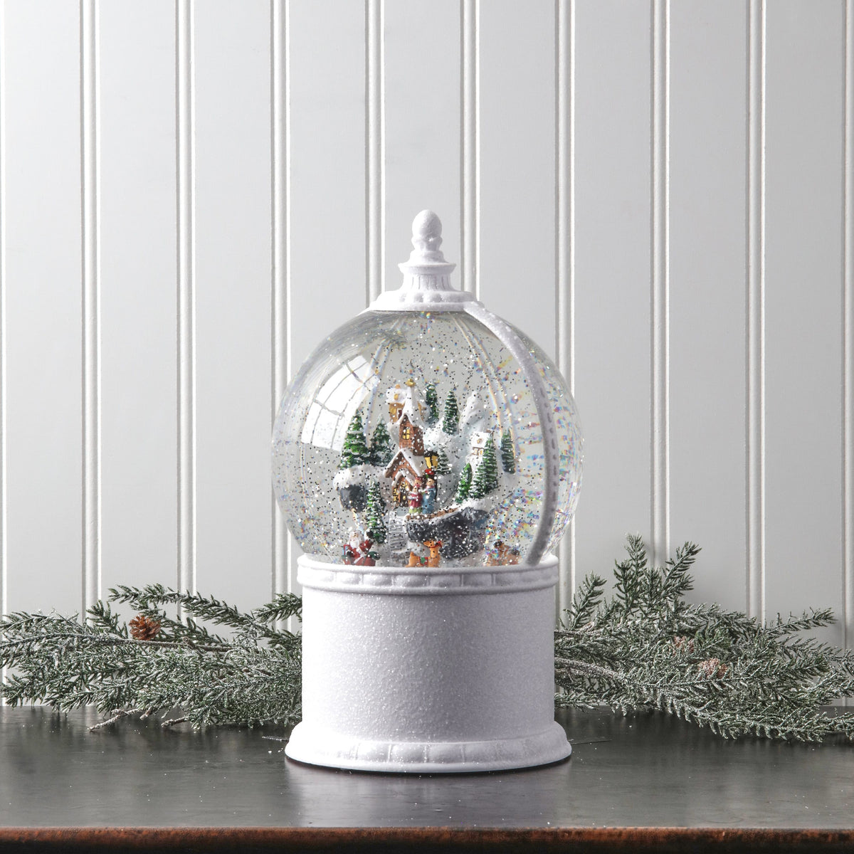 Large snow globe with winter village and Santa scene on white pedestal base, front view