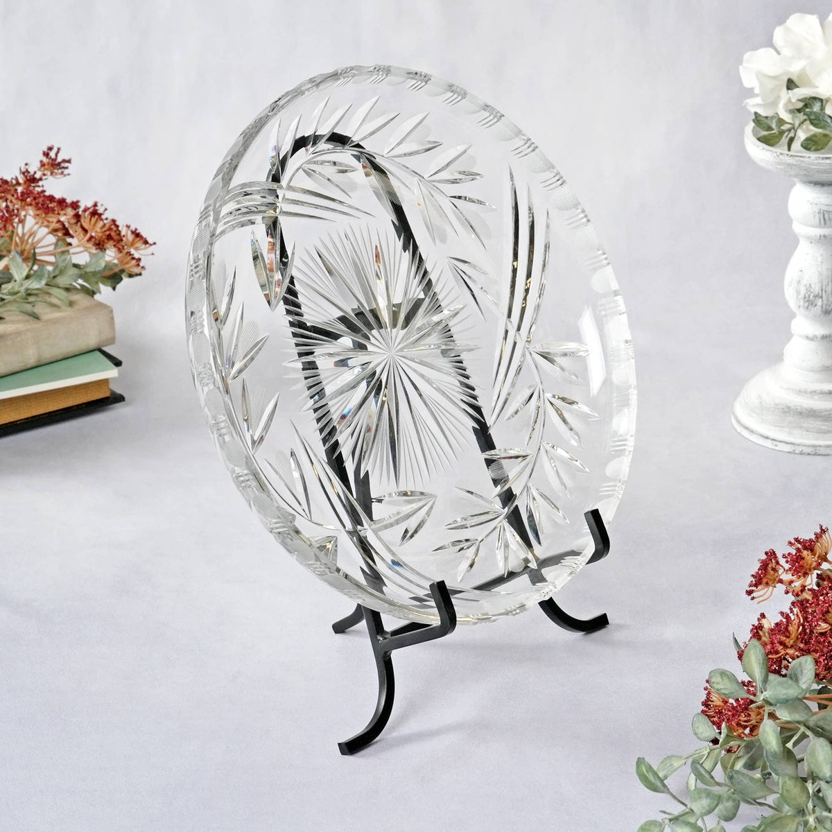 Black wrought iron easel displaying a decorative cut crystal plate on white surface.