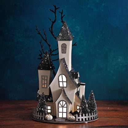 Illuminated cardboard haunted house with black glitter roofs, bare tree, and mini pumpkins on oval base