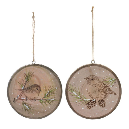 Two round wood slice ornaments with painted birds on snowy pine branches, hanging by twine