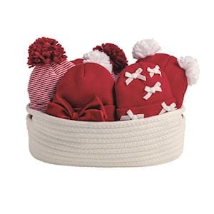 Four red and white baby knit hats with pom-poms in a white rope basket