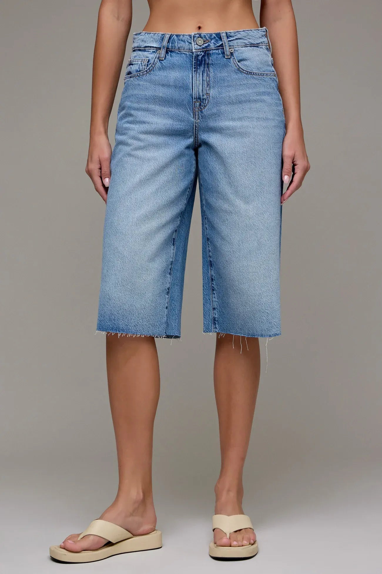 Light blue wash wide-leg denim Bermuda shorts with raw hem and flip flops