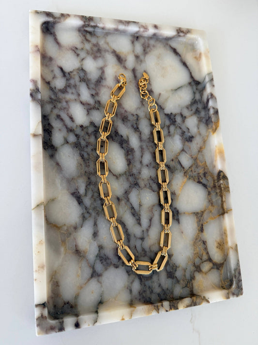 Gold rectangular paperclip chain necklace with lobster clasp on marble tray