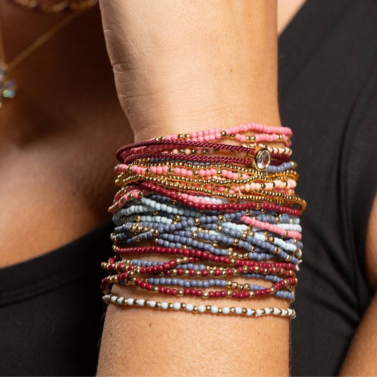 Stacked beaded bracelets in pink, burgundy, blue, and gold on a wrist