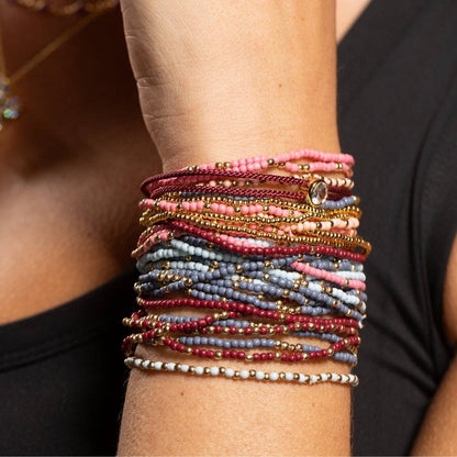 Stacked beaded bracelets in pink, burgundy, blue, and gold on a wrist