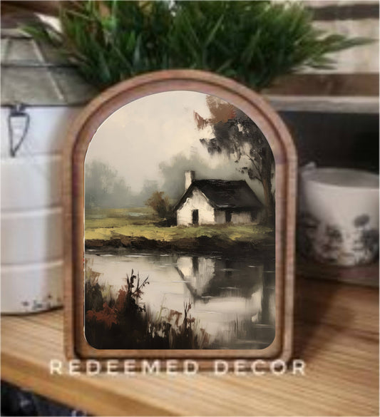 Arch-top wood framed canvas art of a misty cottage reflected in a pond