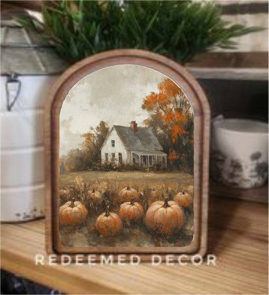 Arched wood-framed canvas art depicting autumn pumpkin patch and white farmhouse