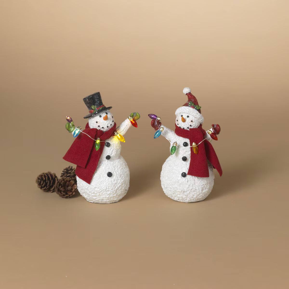 Two white resin snowman figurines with red scarves holding colorful Christmas light strings