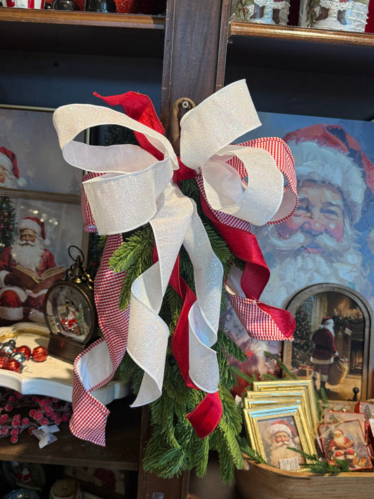 Red and white glitter gingham ribbon bow with evergreen sprigs on wooden shelf