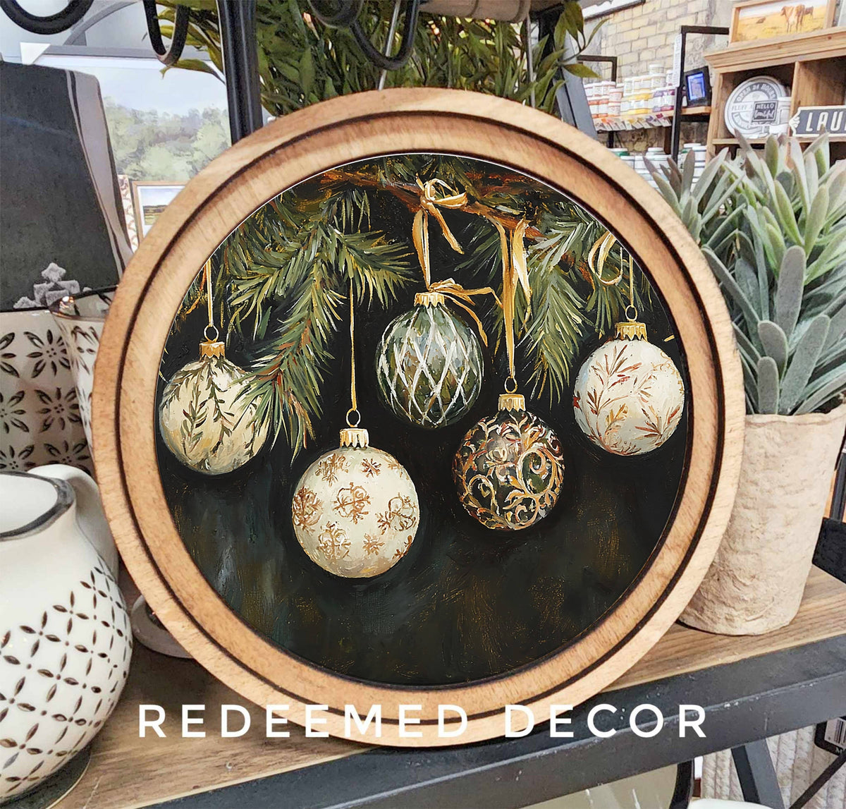 Round wood-framed canvas art with painted Christmas ornaments on pine branches