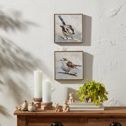 Two framed canvas bird paintings on wall above wooden console with candles and figurines