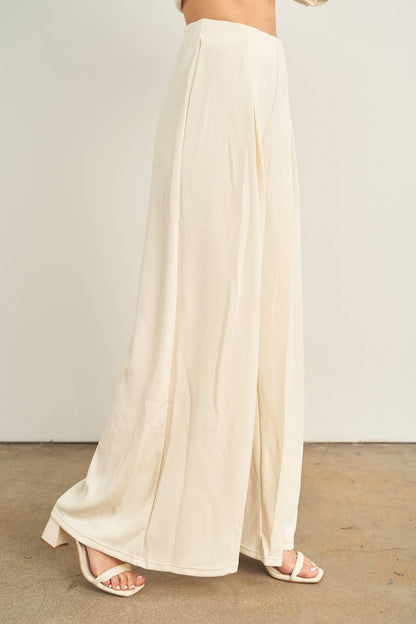 Cream wide-leg palazzo pants with pleated front, worn with white strappy heels
