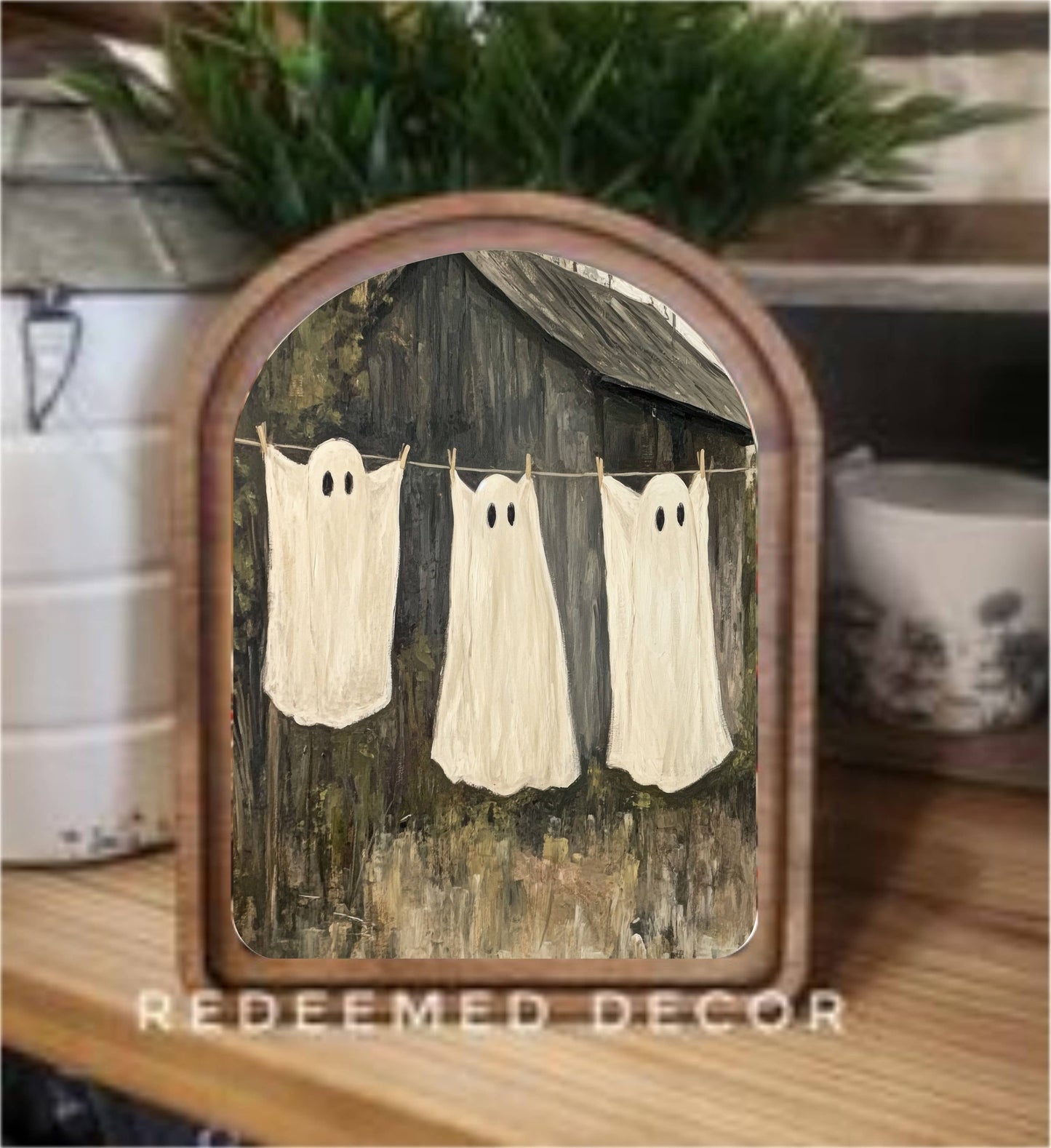 Rustic arched wood framed canvas art with three ghost sheet figures on a clothesline