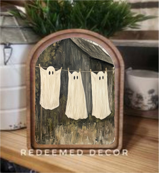 Rustic arched wood framed canvas art with three ghost sheet figures on a clothesline