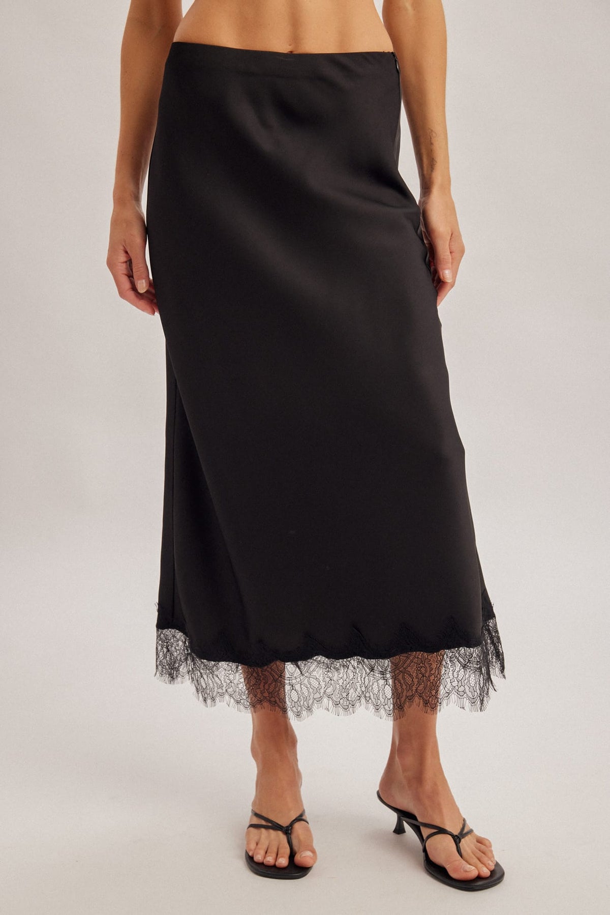 Black satin midi skirt with lace trim hem, low waist, worn with black heeled sandals