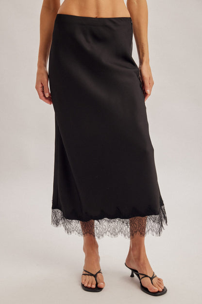 Black satin midi skirt with lace trim hem, low waist, worn with black heeled sandals