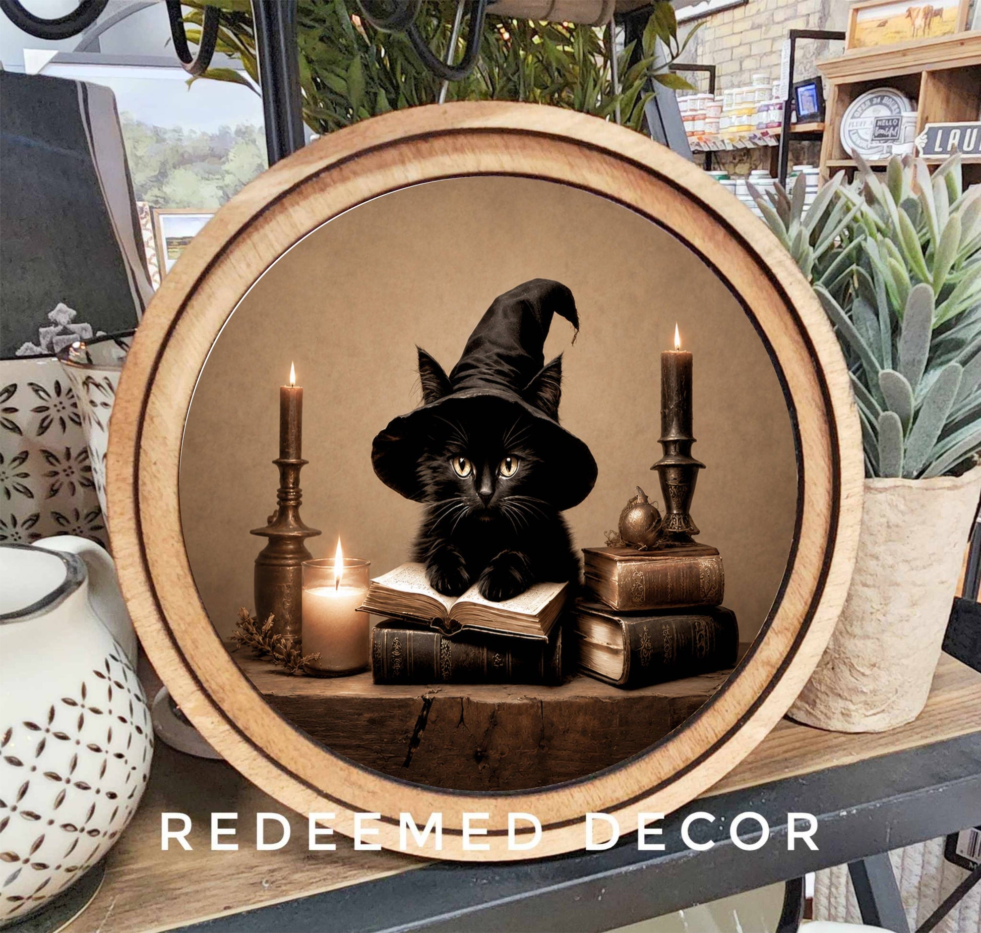 Round wood-framed canvas sign with black witch hat cat, candles, and books
