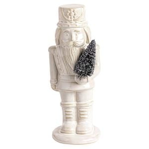 Small white ceramic nutcracker figurine holding a miniature Christmas tree