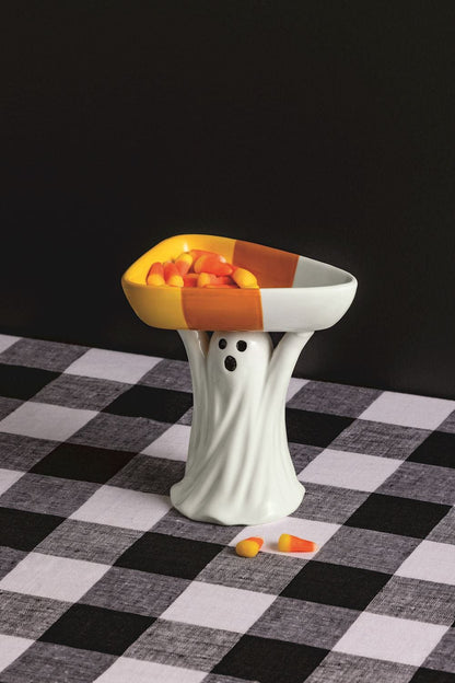 White ceramic ghost figurine holding a candy corn-shaped bowl filled with candy corn