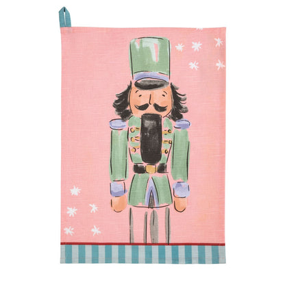 Pink cotton tea towel with illustrated green nutcracker soldier and white snowflakes