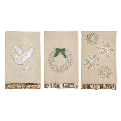 Three beige linen Christmas hand towels with beaded dove, wreath, and snowflake designs, gold fringe trim
