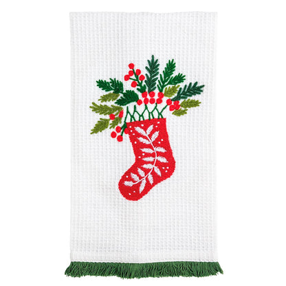 White waffle kitchen towel with embroidered Christmas stocking, holly, and green fringe trim