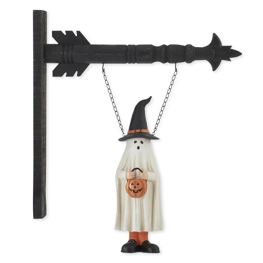 White ghost figure in black witch hat holding pumpkin hanging from black arrow sign bracket