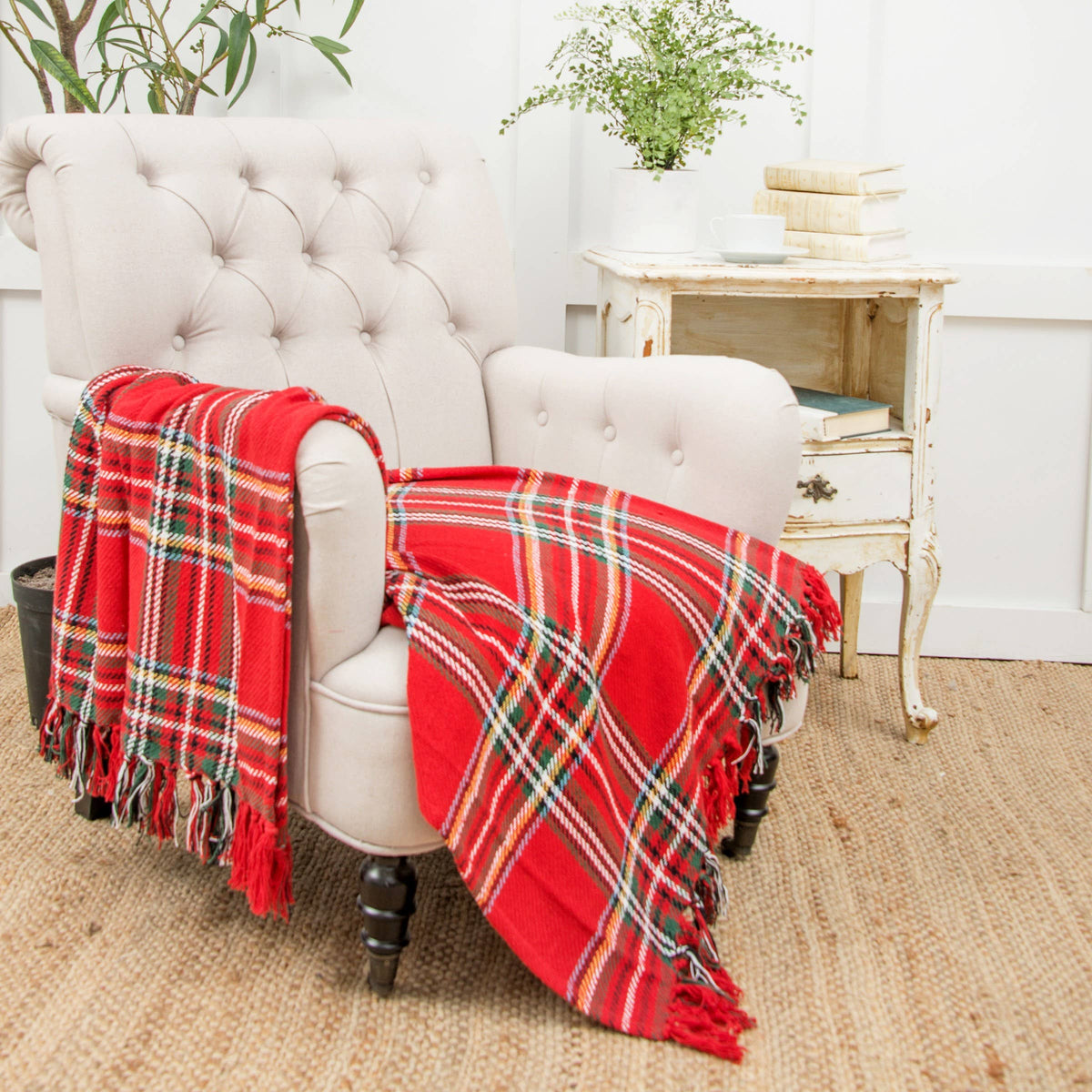 Red tartan plaid cotton throw blanket with fringe draped over cream tufted armchair