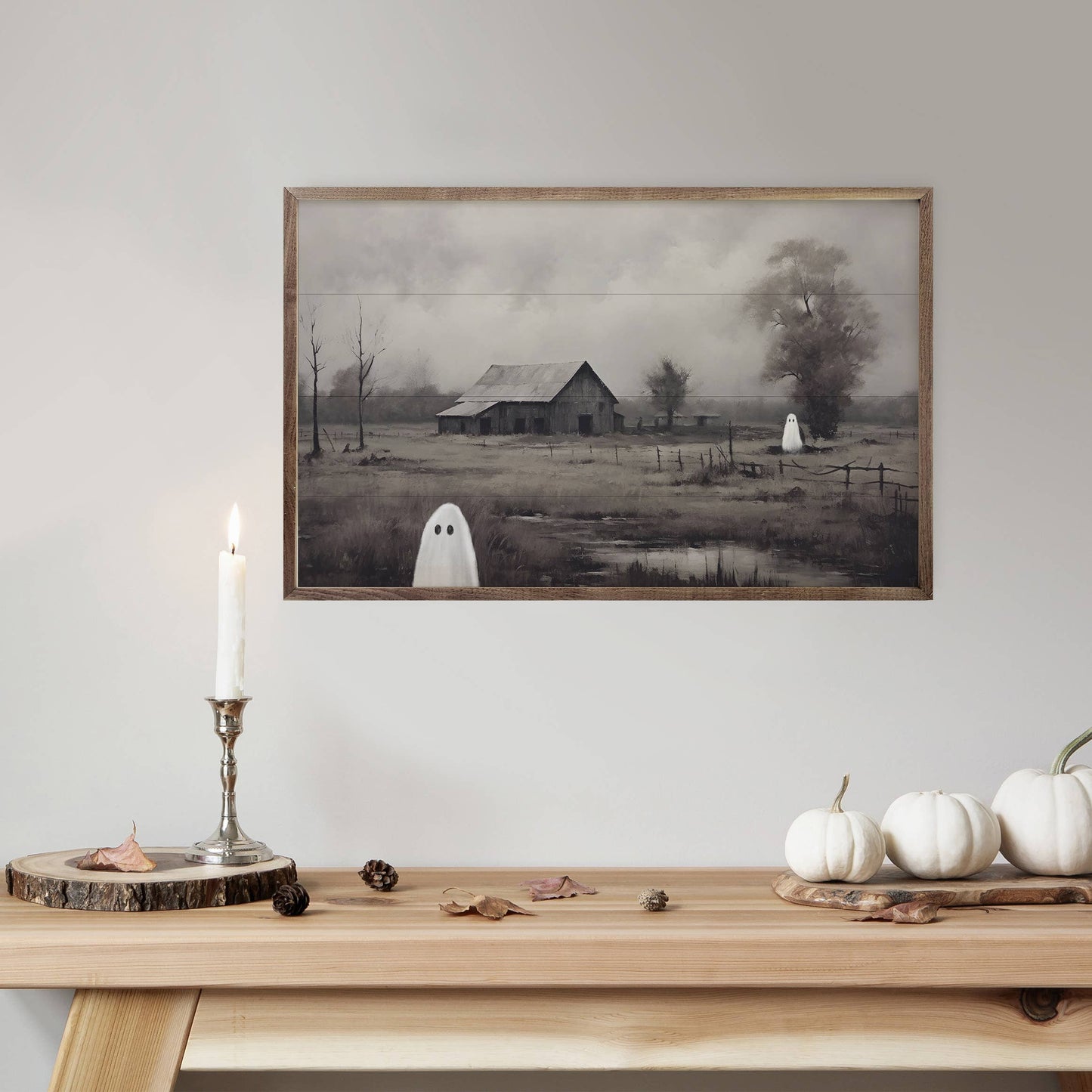 Framed moody Halloween barn painting with ghosts, displayed above wood table with white pumpkins