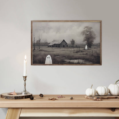 Framed moody Halloween barn painting with ghosts, displayed above wood table with white pumpkins