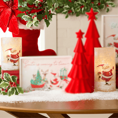 Two frosted cylindrical candle holders with vintage skating Santa illustrations, glowing warmly on a snowy surface