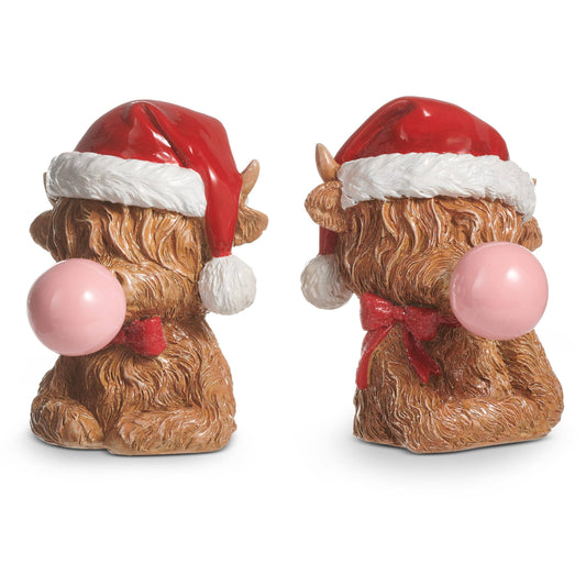 Two views of a fluffy highland cow figurine wearing a Santa hat and blowing a pink bubble