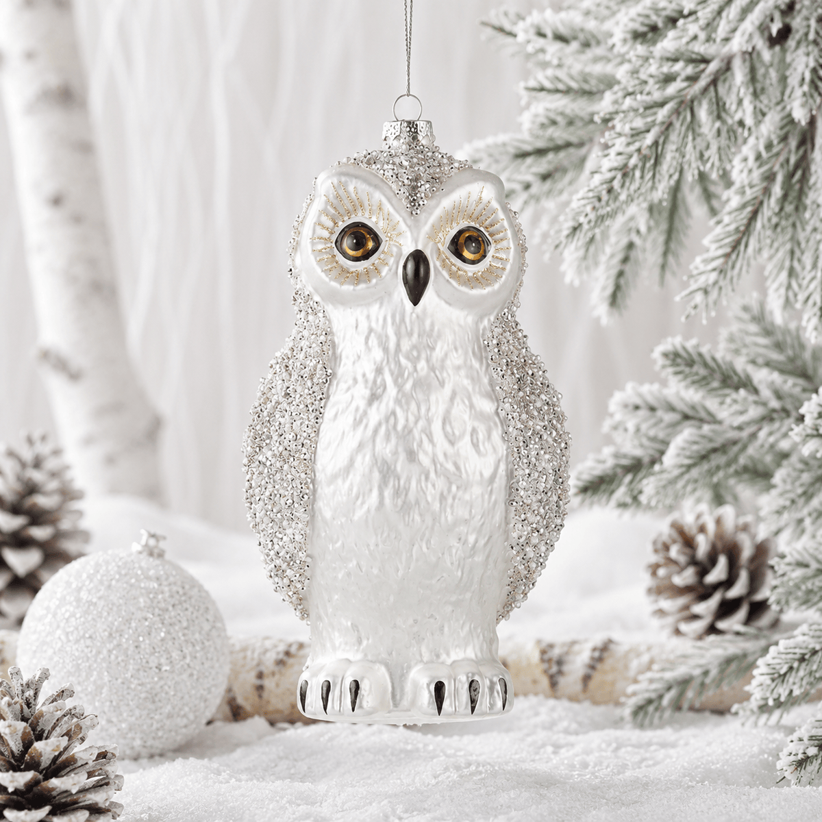 White glass owl ornament with silver beaded wings, gold-accented eyes, and black talons, hanging display