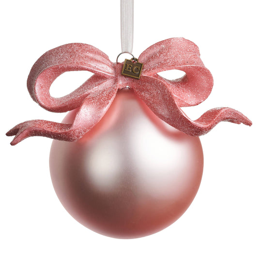 Matte pink ball ornament with glittery pink ribbon bow and small brass charm, hanging view