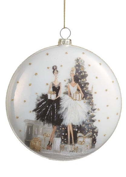 Glass disc ornament featuring two elegant women in black and white gowns by a Christmas tree