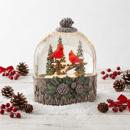 Lighted water globe with two red cardinals on a snowy fence, wood-bark base with pine cones