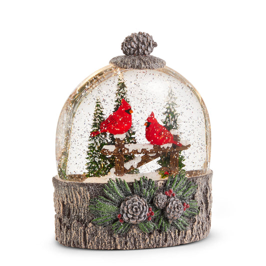 Glass water globe with two red cardinals on a snowy perch, bark-textured base with pinecones