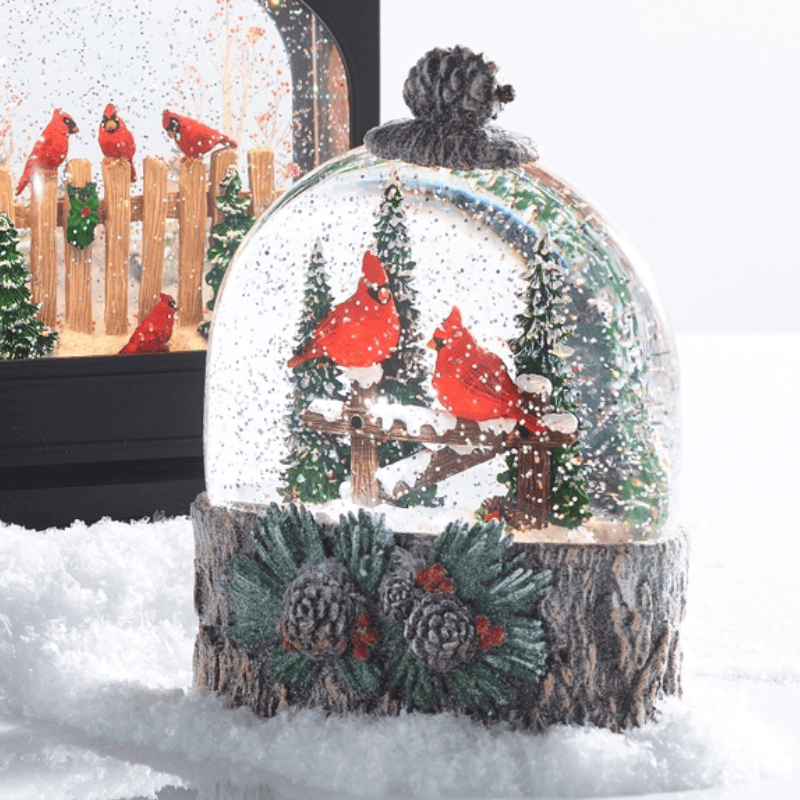 Glass water globe with red cardinal birds on a snowy perch, set on a rustic log base with pinecones