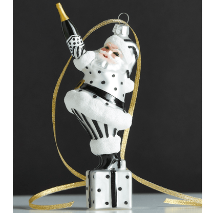 Glass Santa ornament in black and white polka dot suit holding champagne bottle, standing on gift box