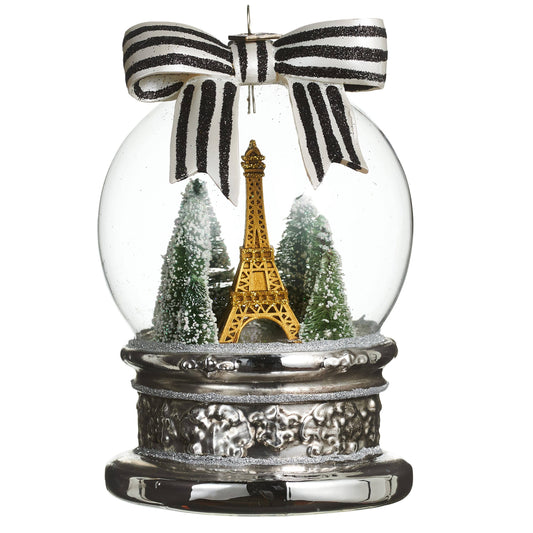 Glass snow globe ornament with gold Eiffel Tower, snowy trees, silver base, and striped bow top