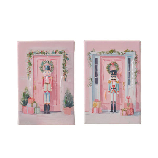 Set of two canvas wall art panels featuring nutcracker soldiers standing before decorated pink doors with Christmas wreaths and gifts