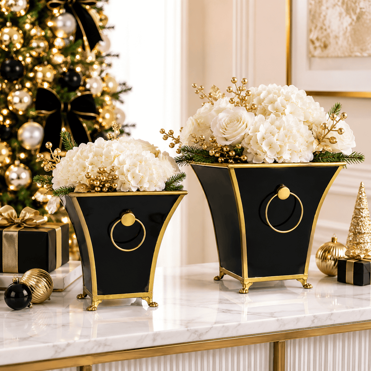 Two black and gold footed cache pots with ring handles filled with white holiday floral arrangements