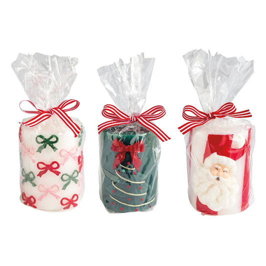 Three Christmas pillar candles in cellophane with red ribbon bows, bows, tree, and Santa designs