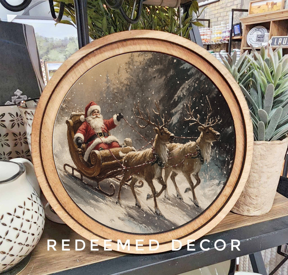 Round wood-framed canvas art of Santa Claus in sleigh pulled by two reindeer in snow